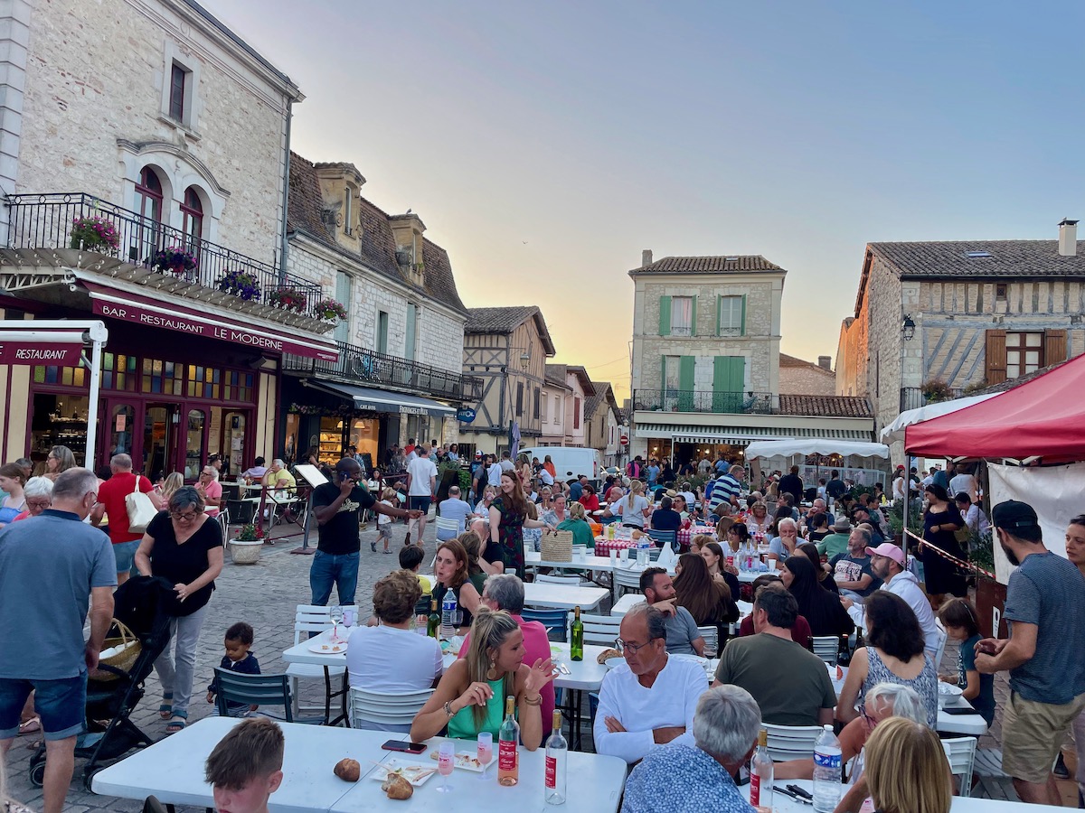 People sitting at tables outside in the town square of Villereal enjoying the night-time food market
