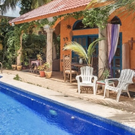 Pool with chairs and orange buildings of Hacienda Boutique Cozumel