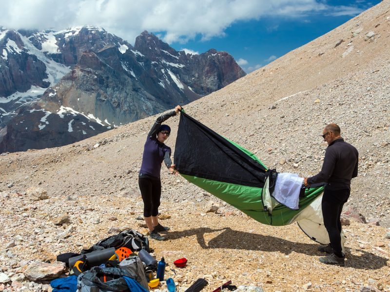 Two people folding a small green bivvi tent on the slopes of a mountain